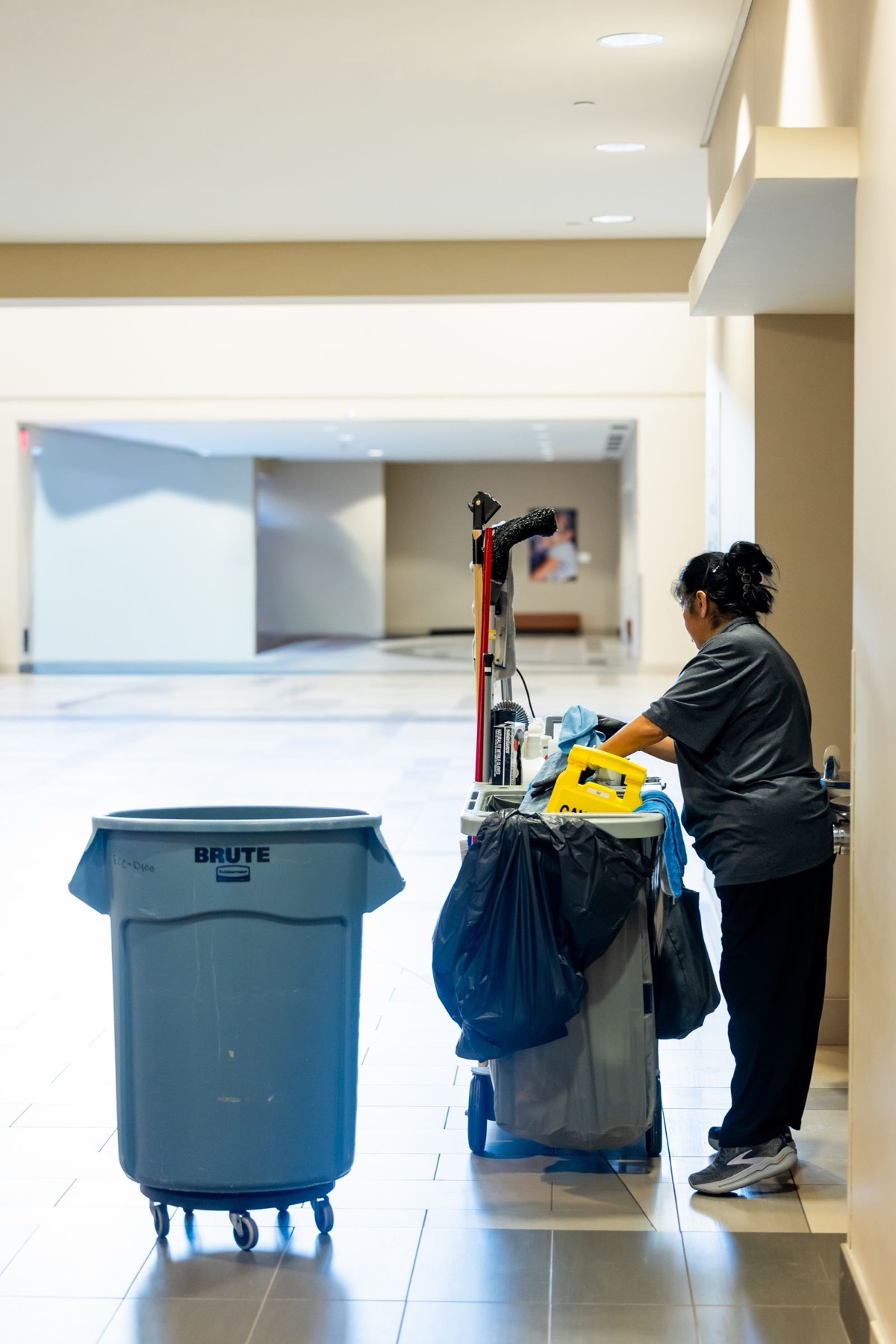 Cleaning cart and cleaner at work in a bright building lobby
