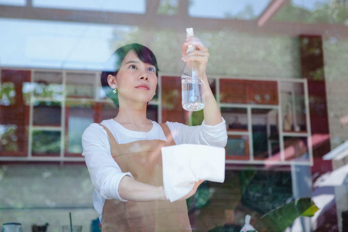 Cleaner wiping common area glass with spray bottle and cloth